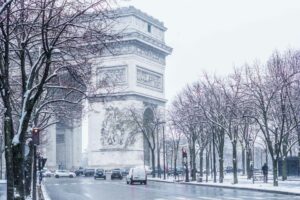 Arc de Triomphe à Paris sous la neige, entouré d'arbres enneigés et d'une rue hivernale.