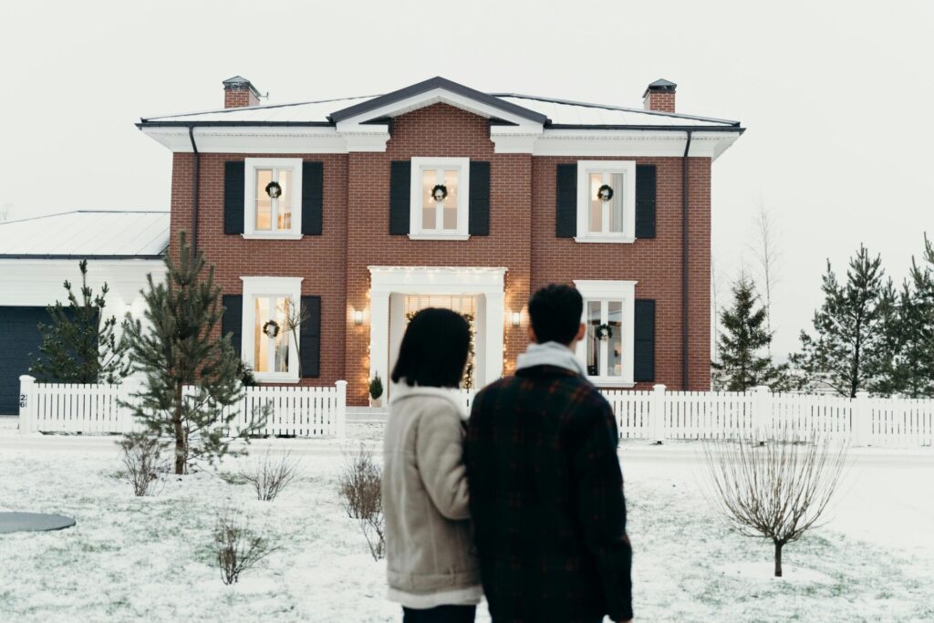 Couple admirant une maison en briques dans un cadre hivernal, prête à être achetée.