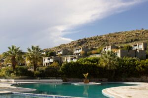 Résidences modernes écoresponsables de luxe entourées de nature, avec une piscine et des palmiers, au pied d'une colline.